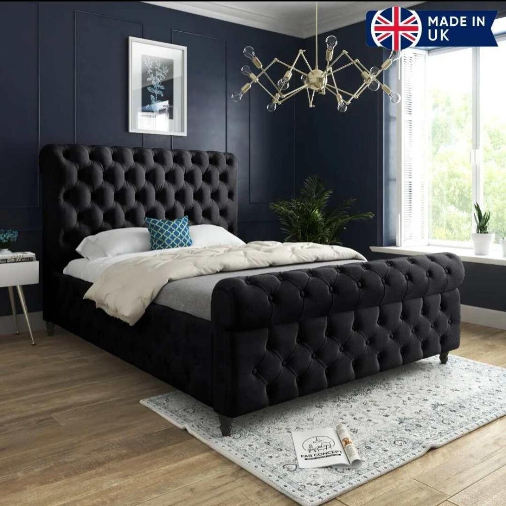 The image shows a Winchester Scroll Bed with a black tufted headboard, neutral bedding, and a blue pillow. Dark blue walls, a floral art piece, and a modern chandelier accent the room. Natural light illuminates plants by the window, with a gray rug labeled "FAB CONCEPT" on the floor. A "Made in UK" badge is in the corner.