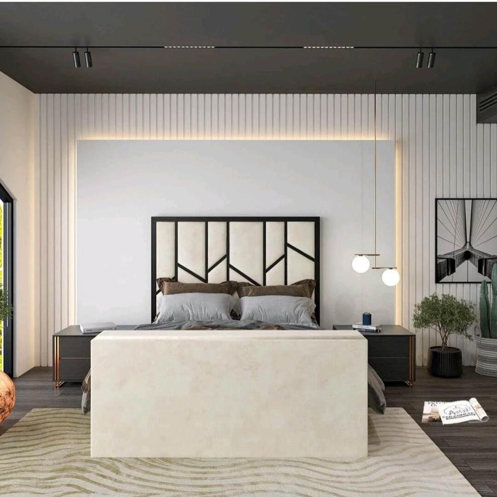 The image depicts a modern bedroom with a Zig Zag TV bed featuring a black-framed geometric headboard and gray pillows. Two sleek dark bedside tables flank the bed, with a book and blue decorative object on the right table under spherical pendant lights.
The minimalist design includes textured vertical white paneling and ambient lighting around the headboard. A light rug with wavy patterns complements the dark hardwood floor.