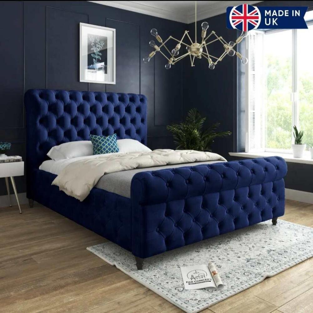 A bedroom with a blue tufted divan bed, modern chandelier, and decorative accents.