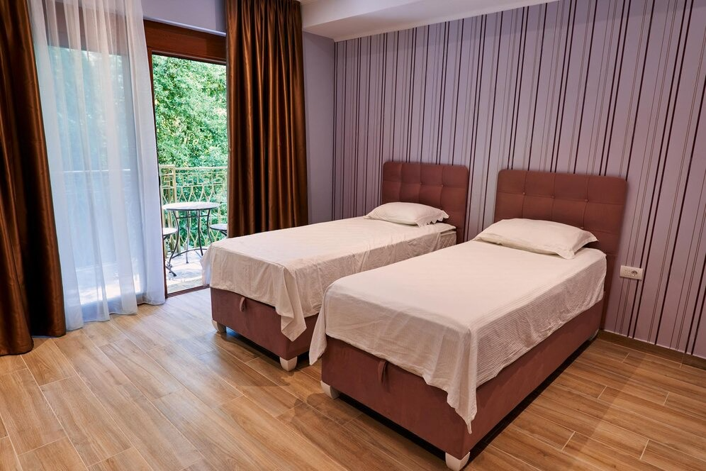 Two single small beds for small room with striped walls and a balcony view.