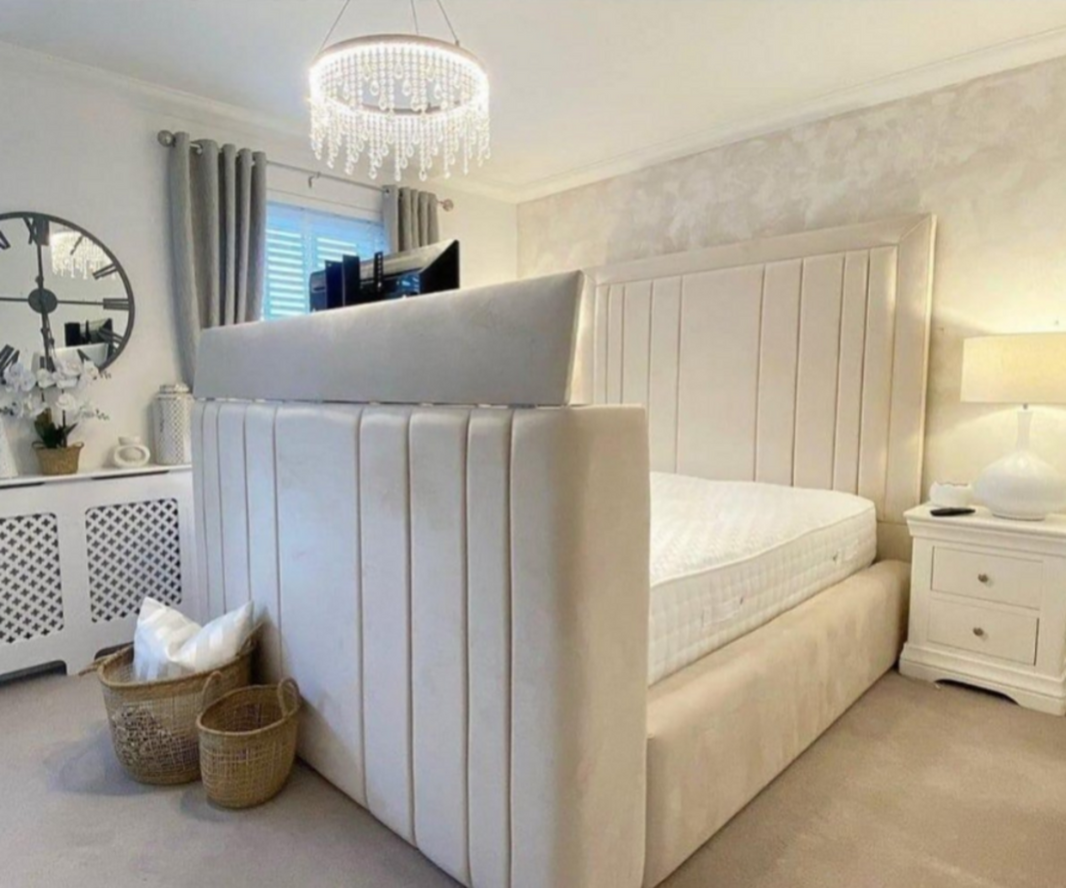 A bedroom with a king size bed and mattress, complete with a padded headboard and footboard in cream fabric, under a crystal chandelier.