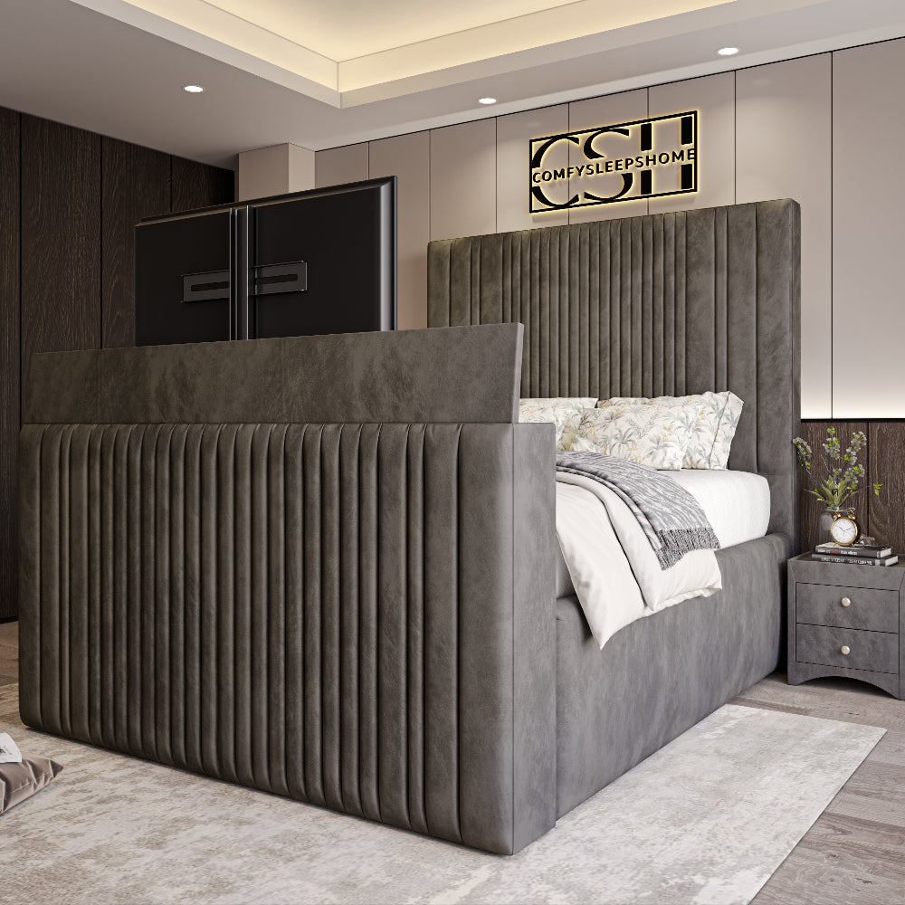 A modern grey 2025 Belgravia TV Bed with a tall, fluted headboard and footboard, featuring a large pop-up television, in a bedroom.