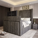 A stately grey 2025 The Astoria TV Bed with a tall, panelled headboard and integrated TV, complementing a modern bedroom interior.