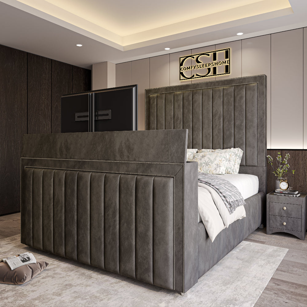 A grand grey upholstered 2025 The Zenith TV Bed with a tall, panelled headboard and integrated TV, featuring subtle stitching in a modern bedroom.
