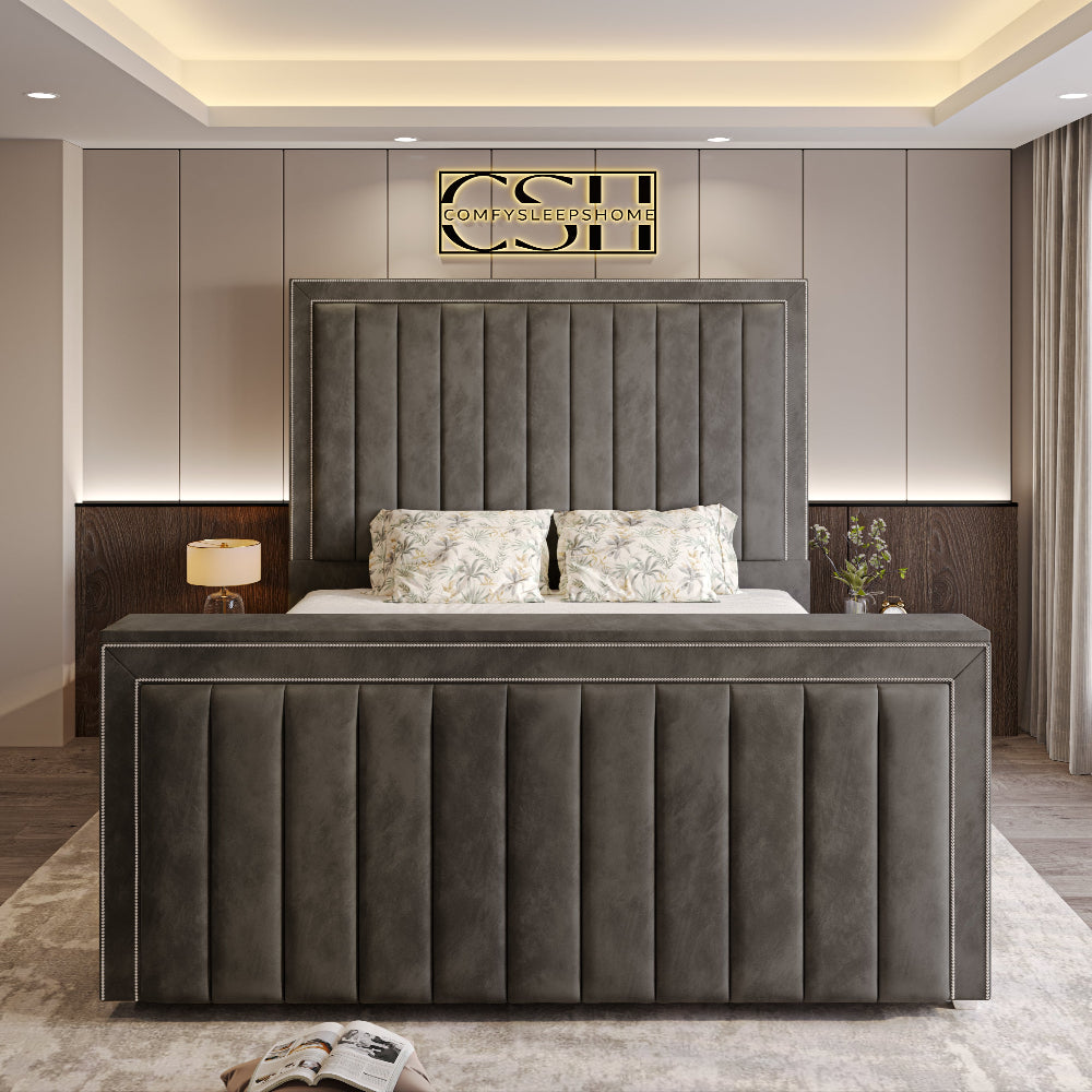 A grand grey 2025 The Zenith TV Bed with a tall, panelled headboard and footboard, featuring elegant studded trim in a modern bedroom.