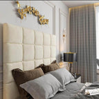 Luxurious bedroom with a creamy white tufted windsor Tv Bed headboard, gray bedding, gold decorative wall art, and a black lamp on a nightstand.

